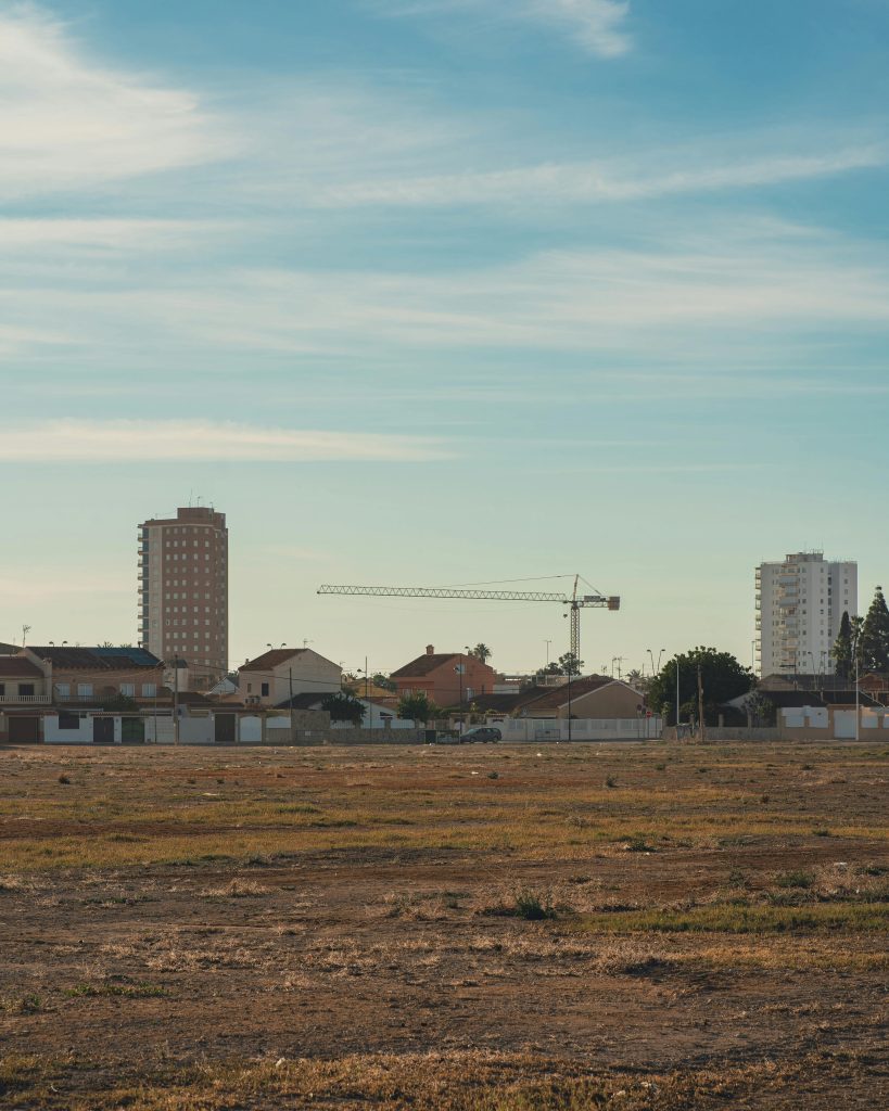 Un paysage urbain avec des bâtiments, des terrains vagues et une grue de construction visible sous un ciel bleu.