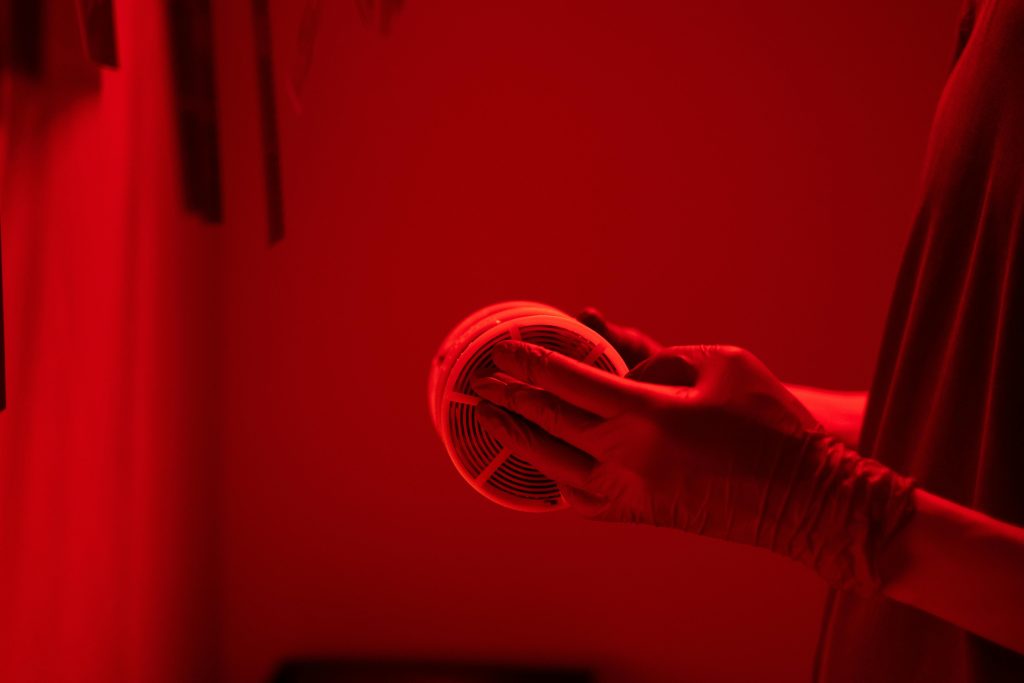 Mains gantées manipulant une bobine de film dans une chambre noire éclairée en rouge, essentiel pour la photographie argentique.