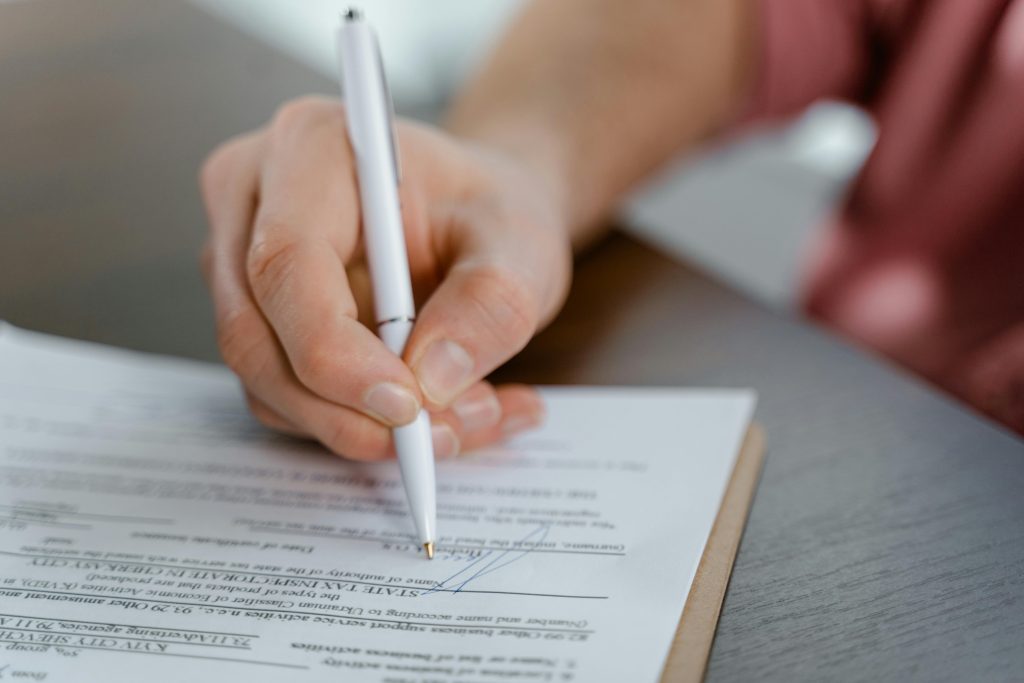 Détail d'une main écrivant une signature sur un document officiel avec un stylo à bille.