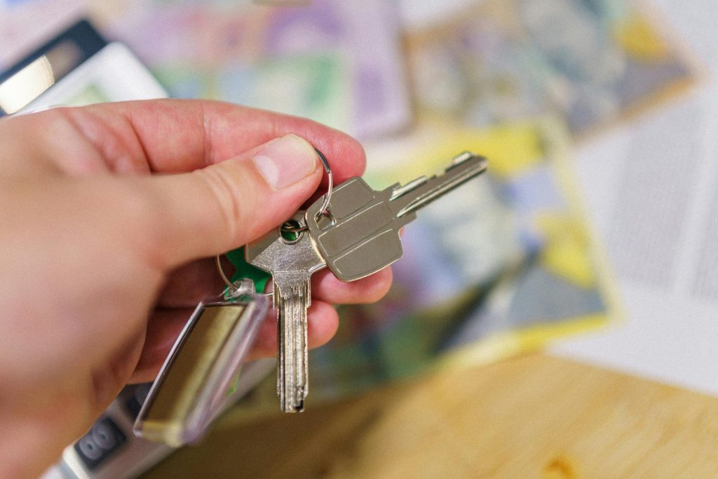 Gros plan de clés dans une main représentant la propriété immobilière avec des documents financiers flous en arrière-plan.