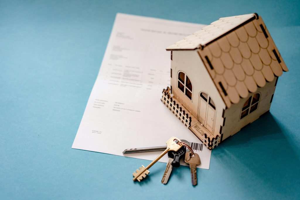 Miniature wooden house with keys and contract symbolizing real estate transactions. Miniature maison en bois avec clés et contrat symbolisant les transactions immobilières.