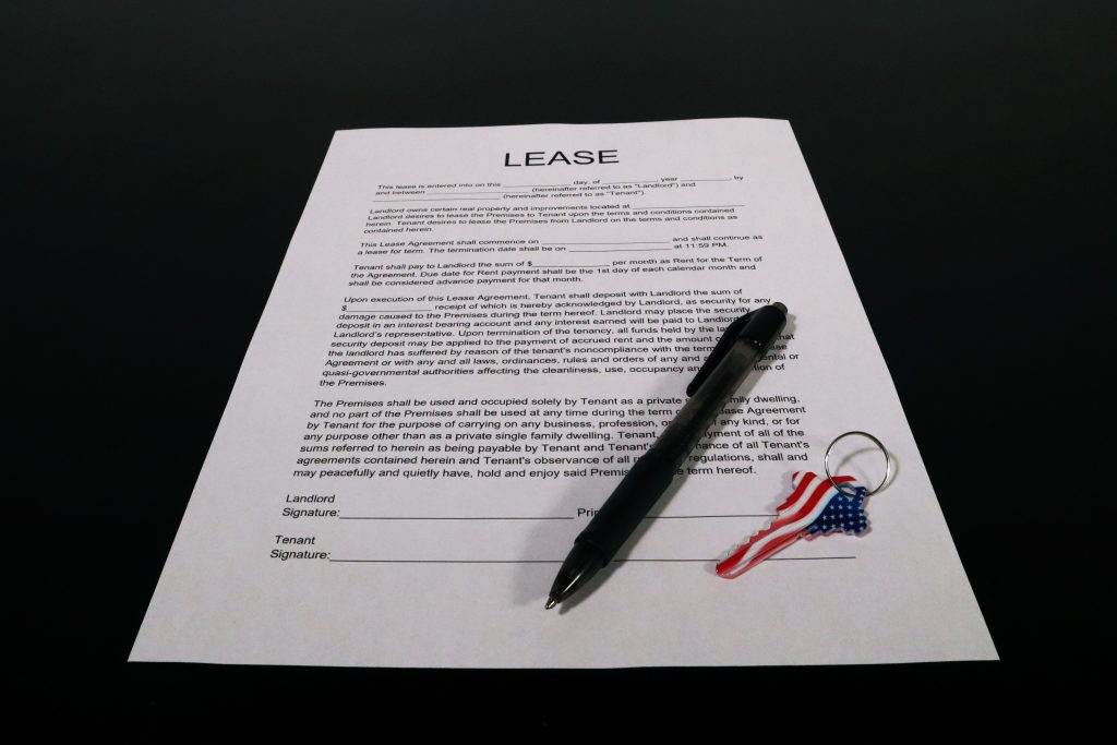 Lease agreement document with pen and American flag keychain on a black table. Document de bail avec stylo et porte-clés drapeau américain sur une table noire.