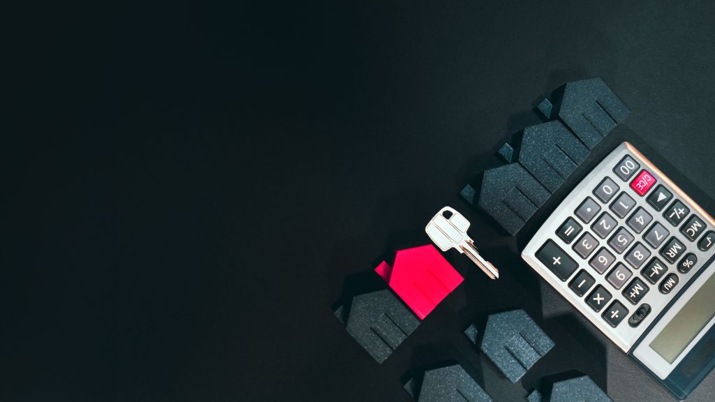 Real estate concept image featuring a calculator, houses, and a key on a black background. Image de concept immobilier présentant une calculatrice, des maisons et une clé sur fond noir.