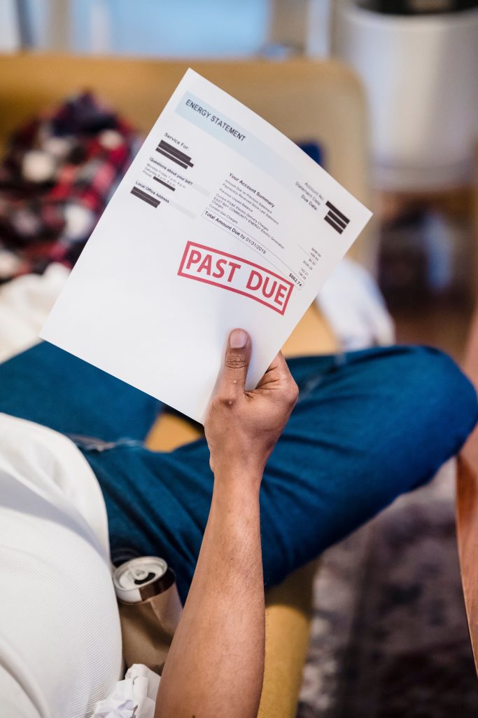 A man holding a past due billing statement while lounging indoors, expressing financial stress. Un homme tenant un relevé de facturation en retard allongé à l'intérieur, exprimant du stress financier.
